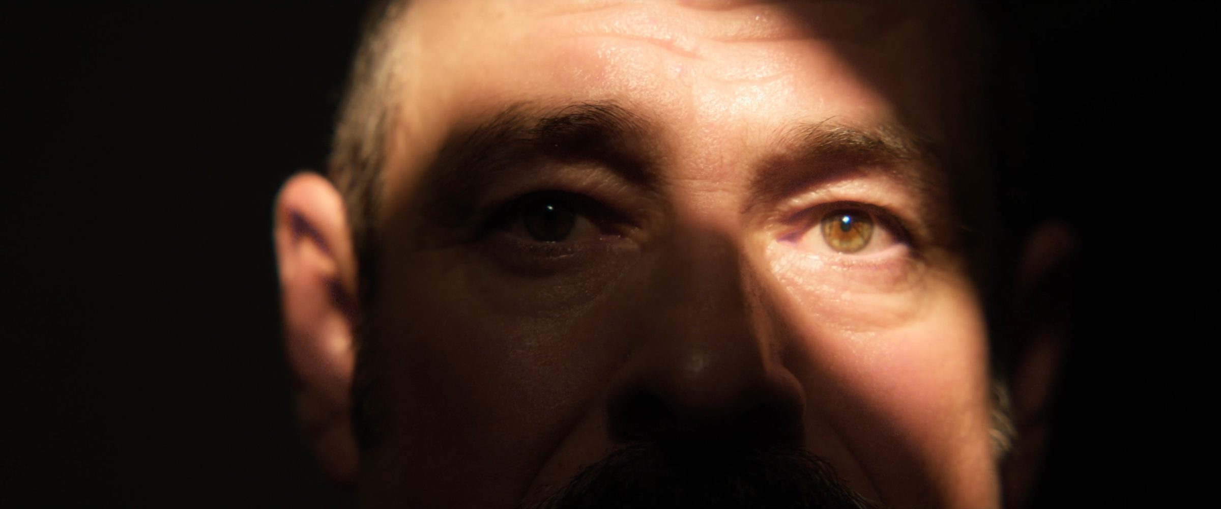 Primer plano de la mirada de un hombre, iluminada por una franja de luz