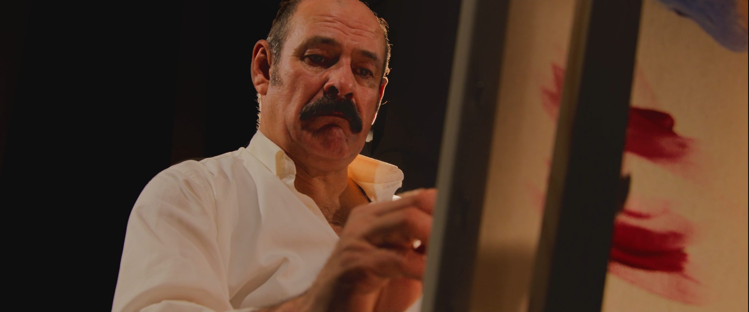 Pintor de bigote trabaja en un lienzo con trazos rojos